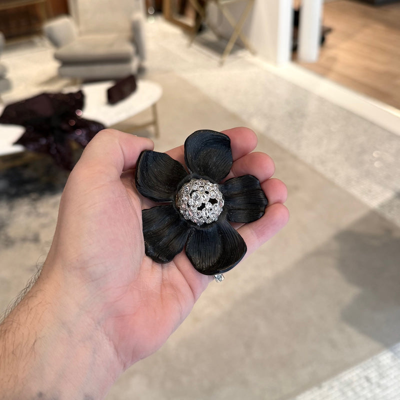 A person holding an Alexis Bittar Crystal Embellished Black Floral Brooch in their hand, showing the size relative to their palm. 