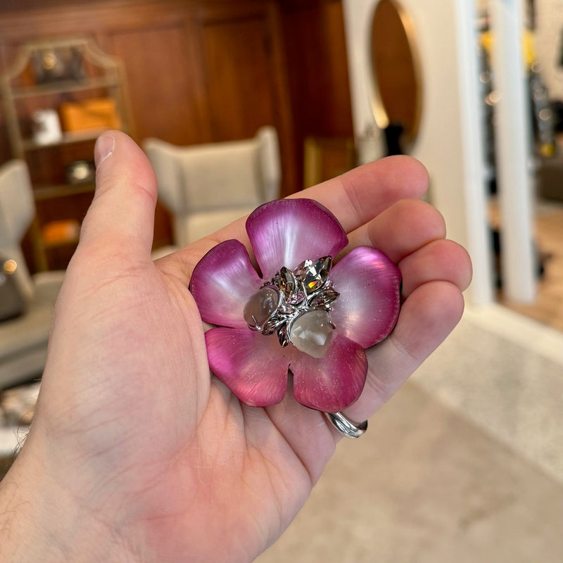 A person holding an Alexis Bittar Crystal Embellished Pink Floral Brooch in their hand, showing the size relative to their palm. 