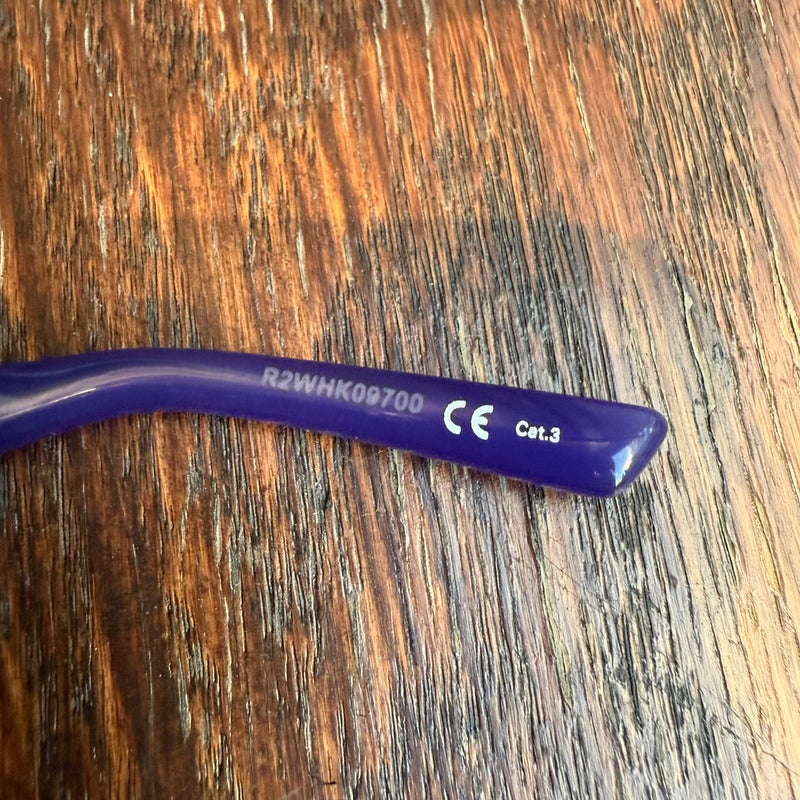 Close-up of the temple tip of Balenciaga BB0096S Purple Dynasty Rectangular Sunglasses, featuring the alphanumeric code "R2WHK09700," CE certification mark, and "Cat.3" UV protection rating printed in white.