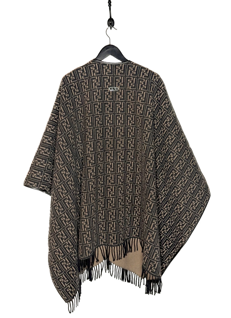 Fendi FF Monogram Leather Trim Wool Fringed Poncho displayed on a hanger. The poncho features an all-over FF monogram pattern in taupe and black, leather trim along the edges, and fringed hems. A silver-tone Fendi logo embellishment is visible at the back. Various images highlight the front, back, close-ups of the fabric, care label, and logo details.