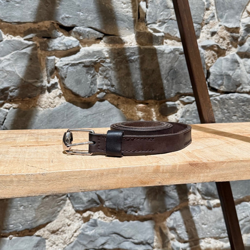 Gucci brown leather belt with silver-tone buckle, embossed branding, and adjustable strap, displayed on a wooden shelf.