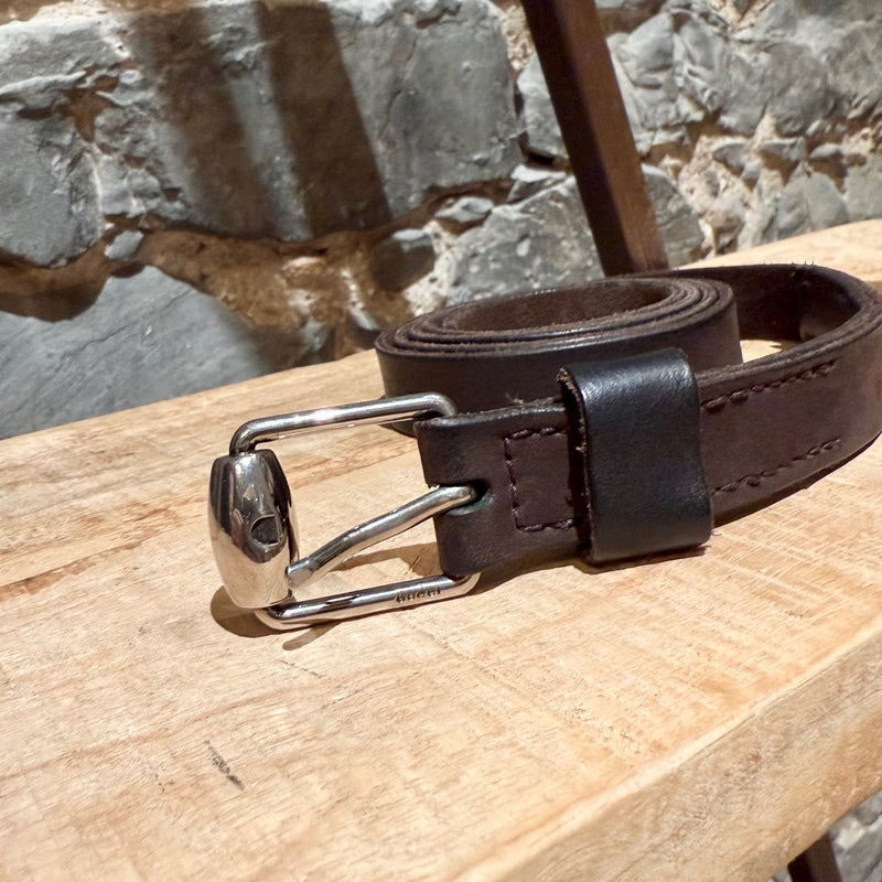 Gucci brown leather belt with silver-tone buckle, embossed branding, and adjustable strap, displayed on a wooden shelf.