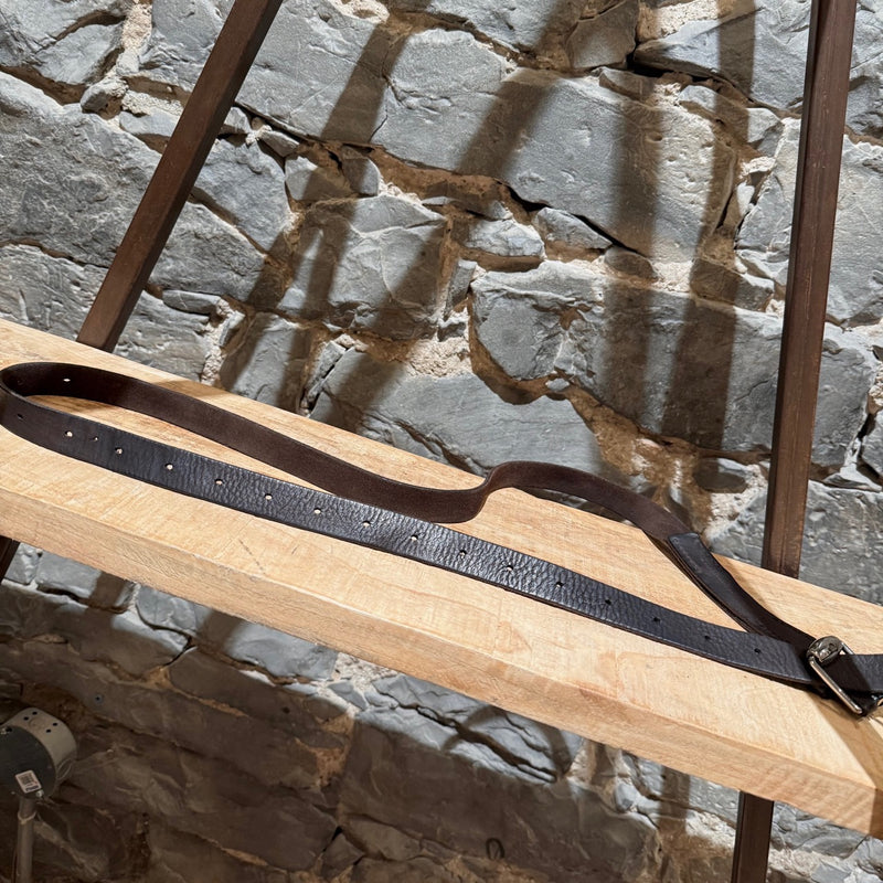 Gucci brown leather belt with silver-tone buckle, embossed branding, and adjustable strap, displayed on a wooden shelf.