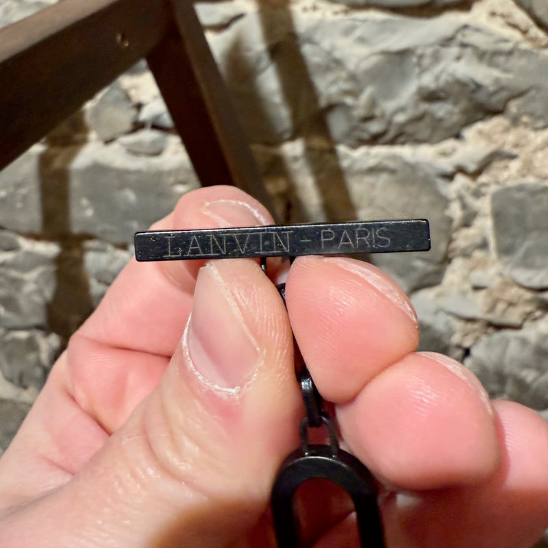 Close-up of the Lanvin Paris logo engraved on a black metal tag, attached to the chain of Lanvin Black Stone Satin Bow Chain Link Necklace