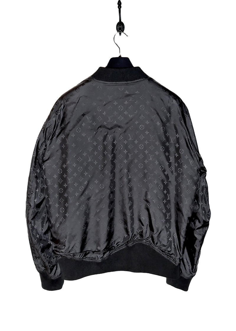 A Louis Vuitton black reversible jacket displayed on a hanger. One side features smooth black leather with ribbed cuffs, collar, and hem, while the other side reveals a black nylon fabric adorned with Louis Vuitton's signature monogram pattern. Close-up shots highlight the premium leather texture, monogram fabric, branded zipper pulls, and the Louis Vuitton logo label. Additional images show the jacket's reversible design, interior details, and stitching.