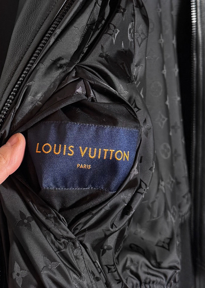 A Louis Vuitton black reversible jacket displayed on a hanger. One side features smooth black leather with ribbed cuffs, collar, and hem, while the other side reveals a black nylon fabric adorned with Louis Vuitton's signature monogram pattern. Close-up shots highlight the premium leather texture, monogram fabric, branded zipper pulls, and the Louis Vuitton logo label. Additional images show the jacket's reversible design, interior details, and stitching.