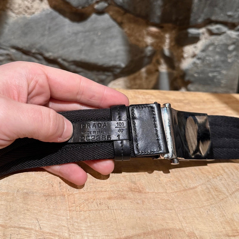 Prada black nylon belt with a silver-tone logo-engraved slide buckle, shown from various angles to highlight details such as the material, buckle engraving, and overall design.