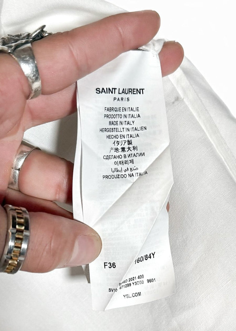 Saint Laurent YSL Logo White Linen Blend Buttoned Shirt. A white button-up shirt featuring a pointed collar, tonal embroidered YSL logo on the chest pocket, and engraved buttoned cuffs. Made in Italy, crafted from a linen-cotton blend, with a clean and lightweight silhouette.