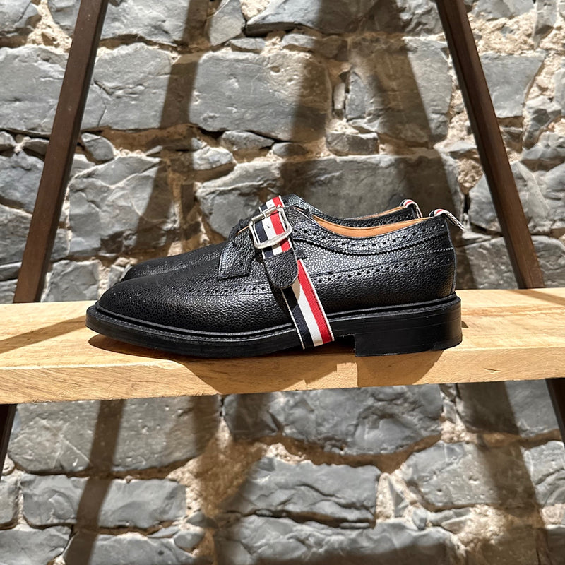 A side view of Thom Browne Black Pebbled Grosgrain Tricolour Strap Long Wingtip Shoes