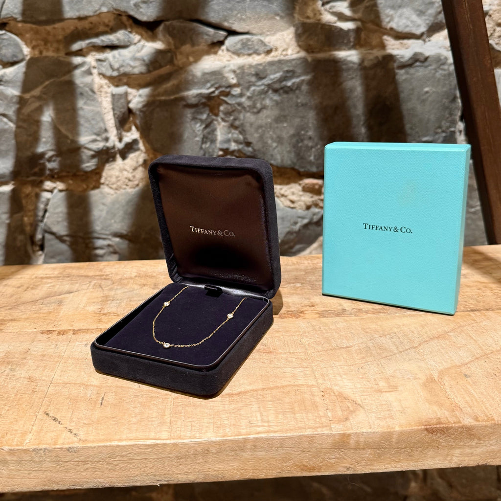 A close-up of the Tiffany & Co. necklace inside its black velvet jewelry box, with the Tiffany blue box placed next to it on a wooden surface.