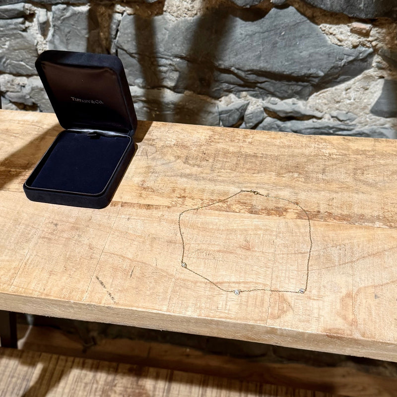 A Tiffany & Co. necklace with three diamond stations displayed on a rustic wooden surface, alongside the black jewelry box.