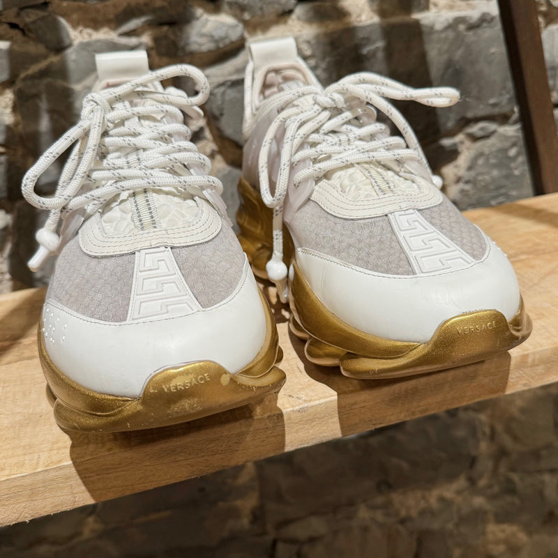 Versace White Gold Chain Reaction Sneakers featuring a white upper with translucent panels, textured fabric, embossed Greca patterns, and a bold gold chain-link sole. Includes Medusa head detailing on the heel and 'Chain Reaction' emblem on the tongue, with rope-style laces and pull tabs.