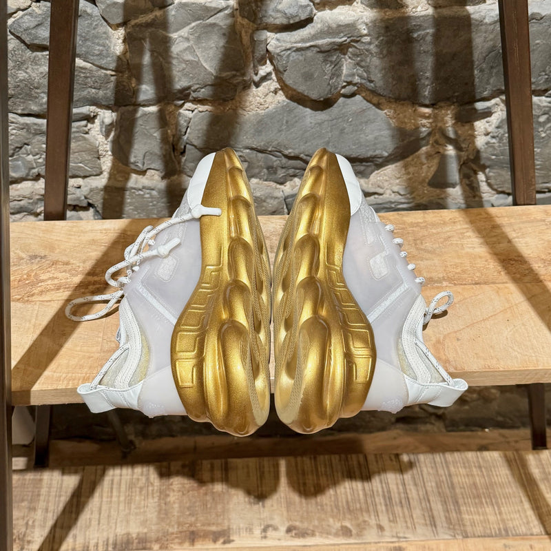 Versace White Gold Chain Reaction Sneakers featuring a white upper with translucent panels, textured fabric, embossed Greca patterns, and a bold gold chain-link sole. Includes Medusa head detailing on the heel and 'Chain Reaction' emblem on the tongue, with rope-style laces and pull tabs.